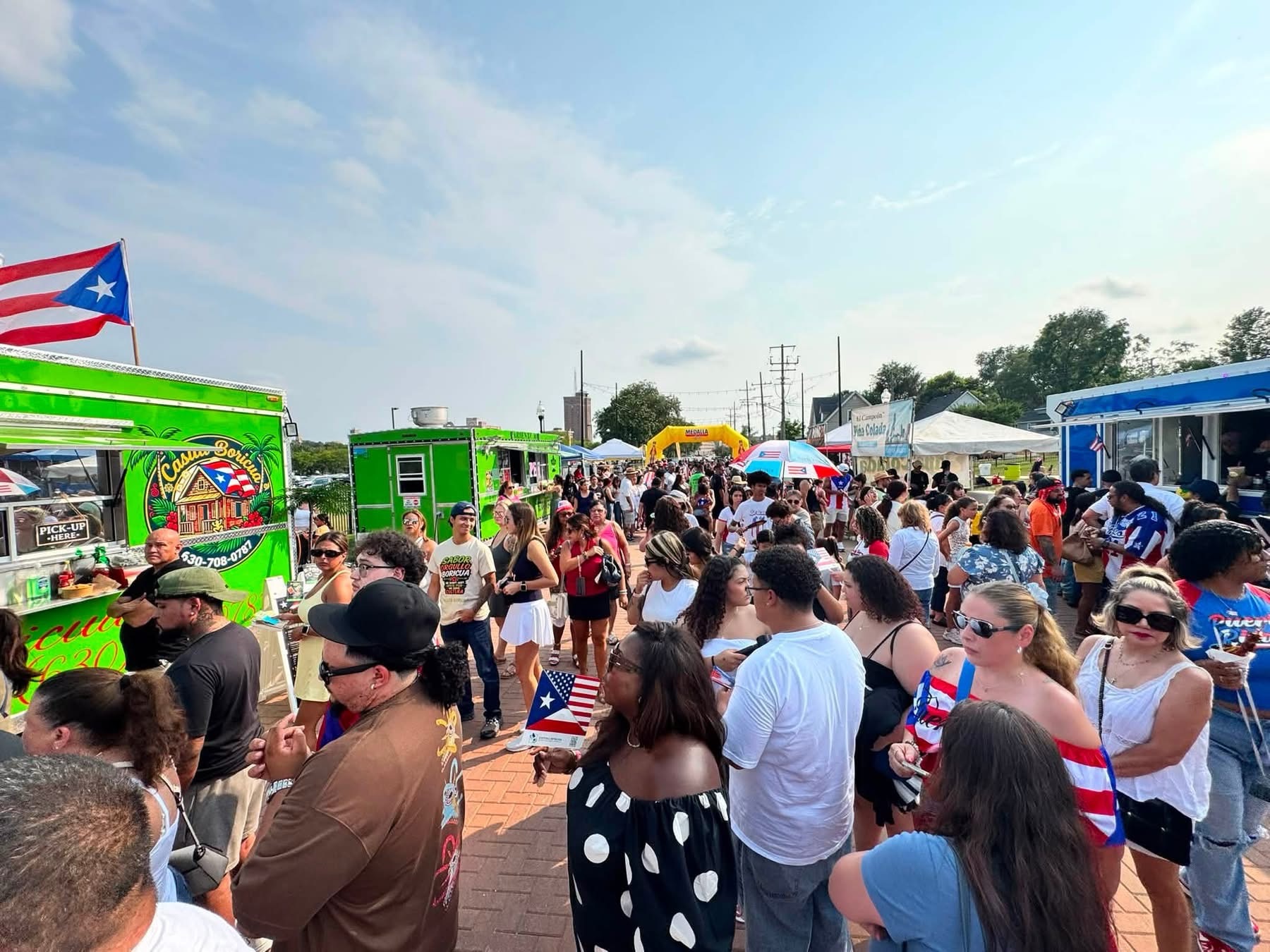 Festival guests gathering among food vendors under a Puerto Rican flag at Wilder Park