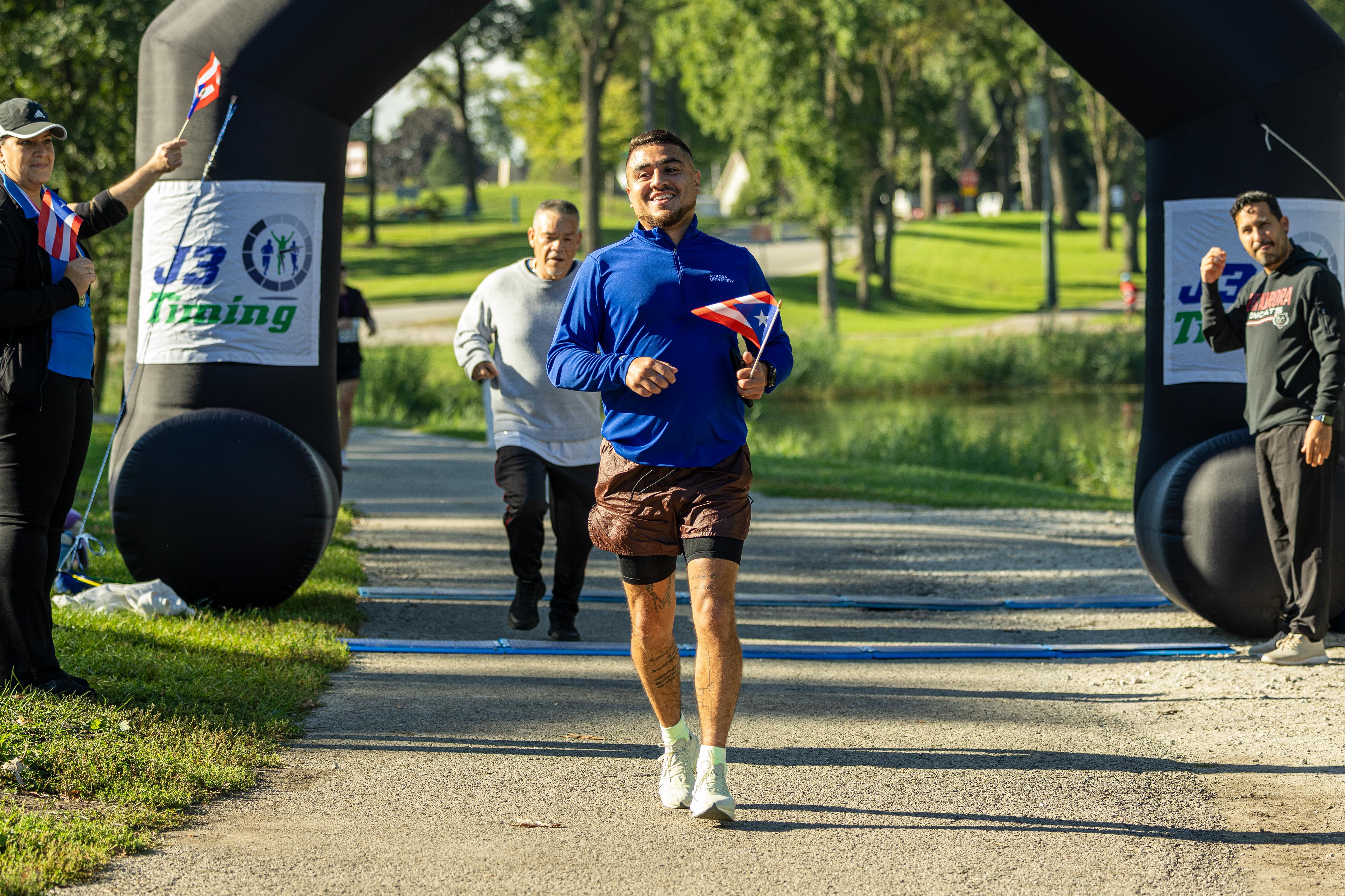 A Coquí 5K runner crossing the finish line with a Puerto Rican flag